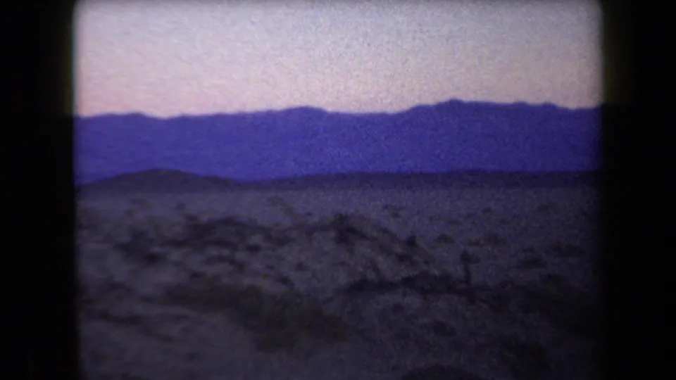 1958 Arizona 8mm frame with scrubby desert ground, a broad mountain range, and low-light color shift near dusk.