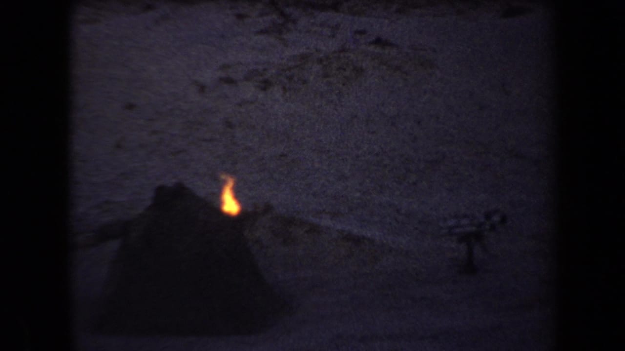Small flame burning near a dark tent-like shape on desert ground.