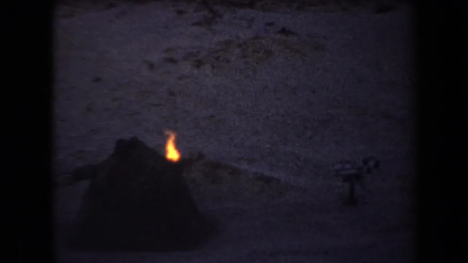 Arizona 1958 8mm frame showing a small campfire beside a dark tent-like shape in a dusk desert setting.