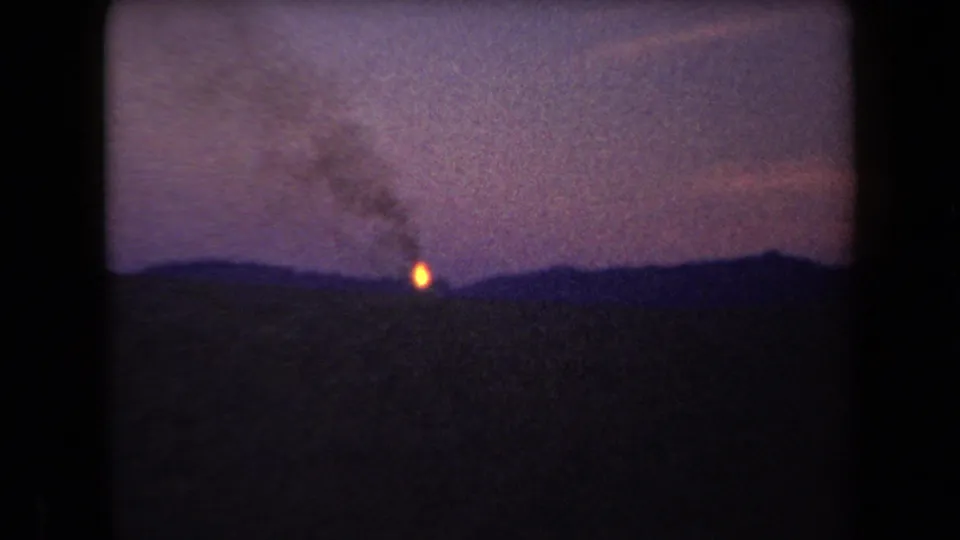 Arizona 1958 8mm frame showing a distant bright fire or flame on the horizon with smoke lifting into a purple dusk sky.