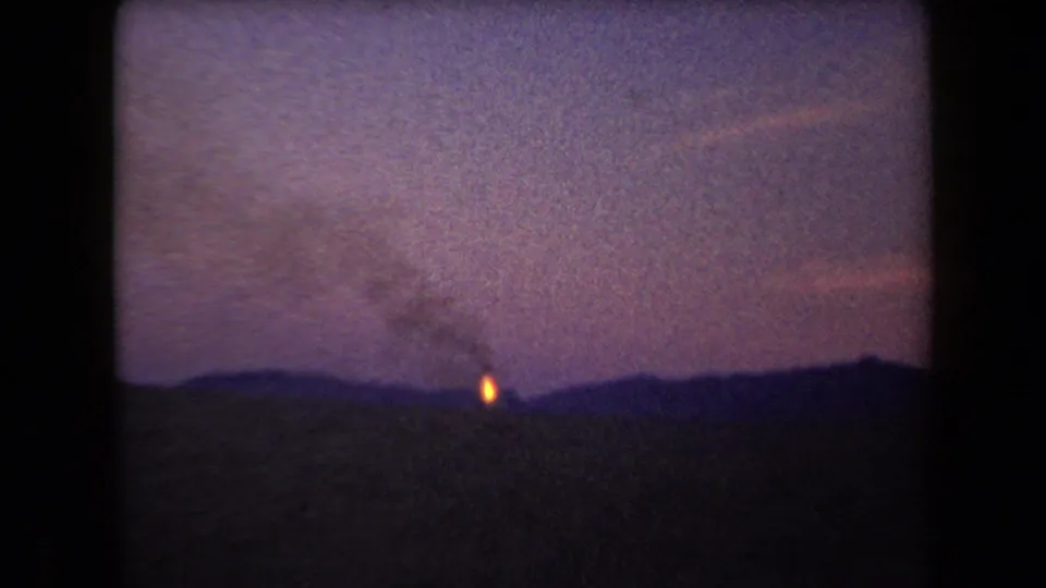 1958 Arizona 8mm frame showing the fire slightly lower in the composition, under smoke and a grainy dusk sky over mountains.