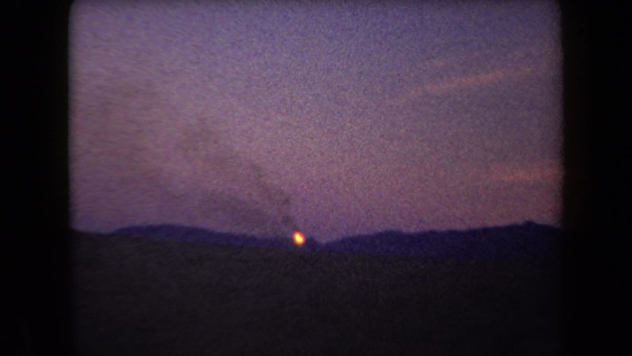 1958 Arizona 8mm frame showing a small distant fire and faint smoke against silhouetted hills at dusk.