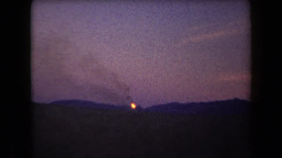 1958 Arizona 8mm frame showing a small distant fire and faint smoke against silhouetted hills at dusk.