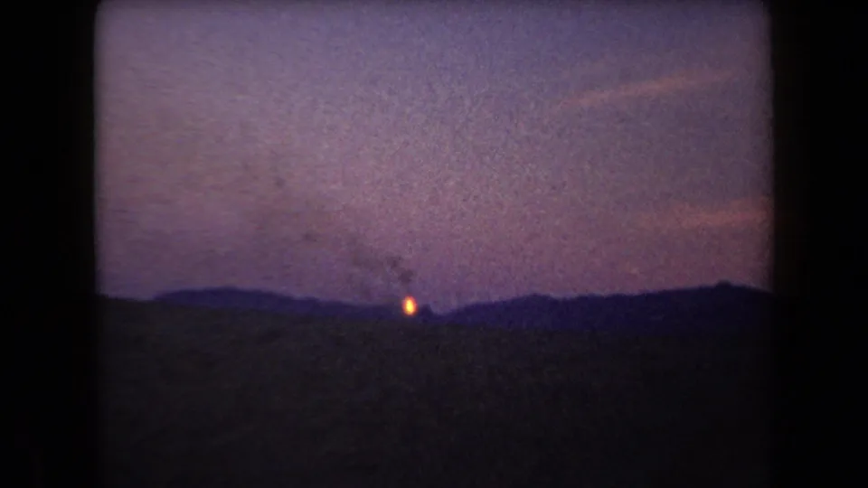 1958 Arizona 8mm view of a distant hillside fire with smoke rising into a dim purple sky.