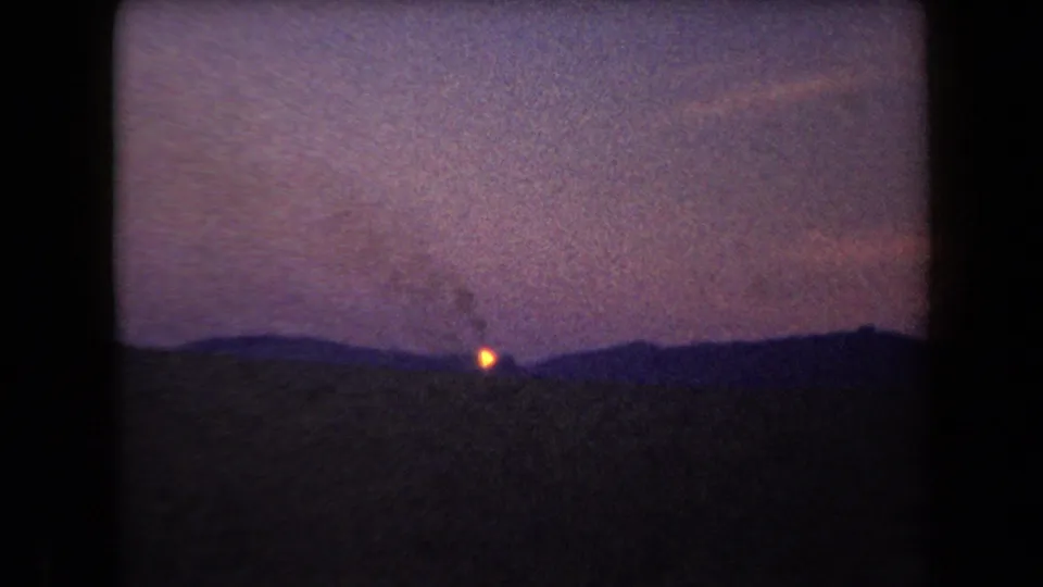 1958 Arizona home-movie frame with a small fire on a distant hill and smoke visible above it.