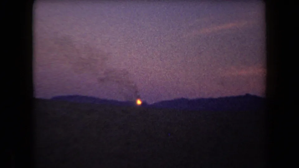 1958 Arizona 8mm frame showing a distant hillside fire at dusk with smoke softened by film grain.