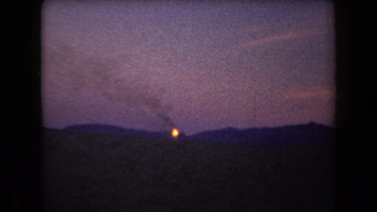 1958 Arizona 8mm frame showing a tiny orange ignition on a silhouetted horizon under a purple dusk sky.