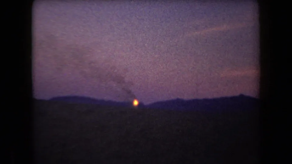 1958 Arizona 8mm frame showing a tiny orange ignition on a silhouetted horizon under a purple dusk sky.