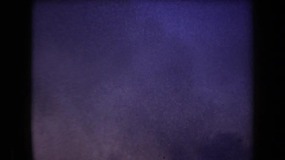 Final 1958 Arizona 8mm frame with purple-blue grain, dark side border, and faint shadowed terrain or haze near the bottom.