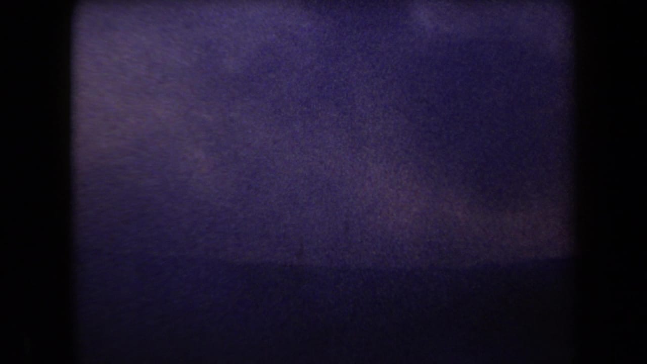 1958 Arizona 8mm frame with purple color shift, heavy grain, dark borders, and faint horizontal banding.