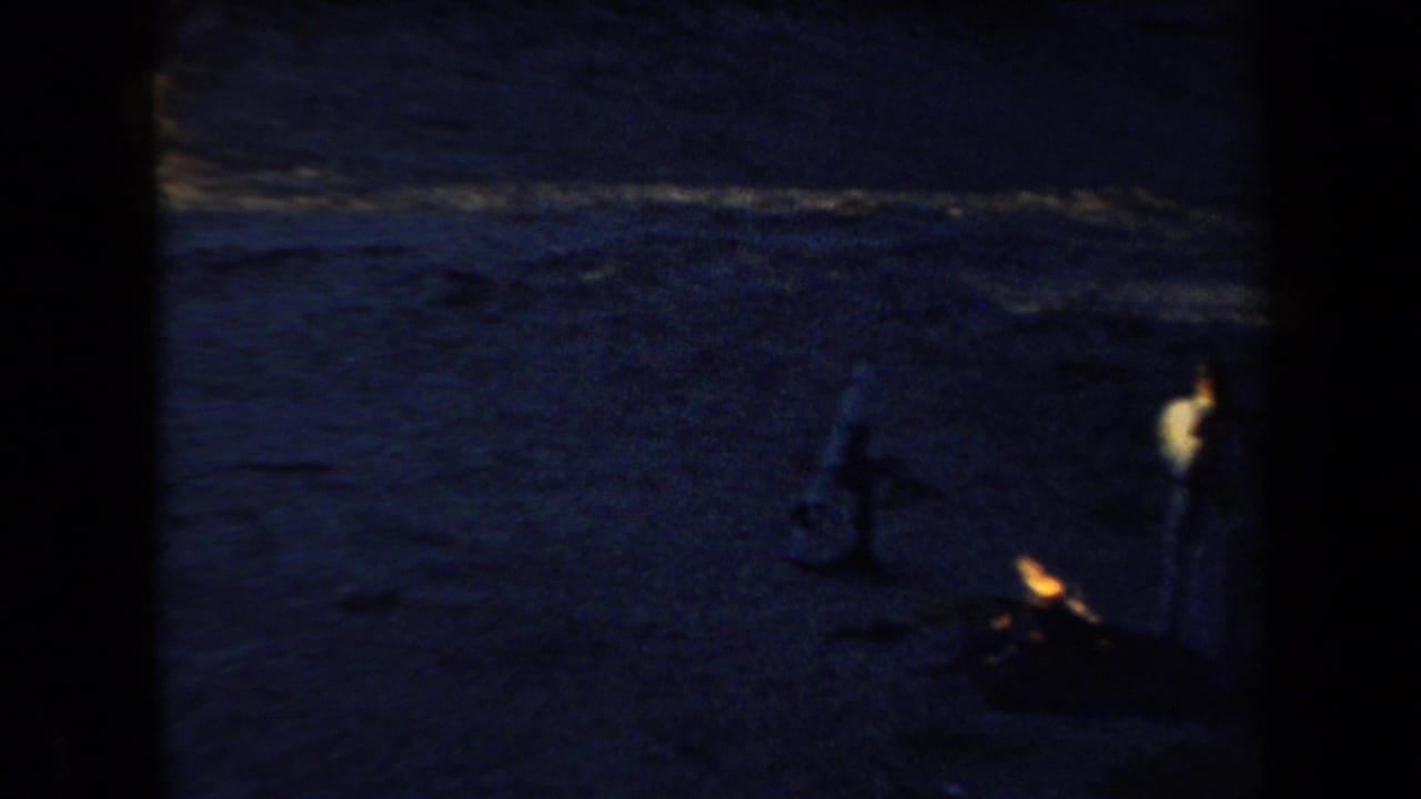Low-light 1958 Arizona campsite view with dark sand and a small warm fire or lamp glow near the right side.