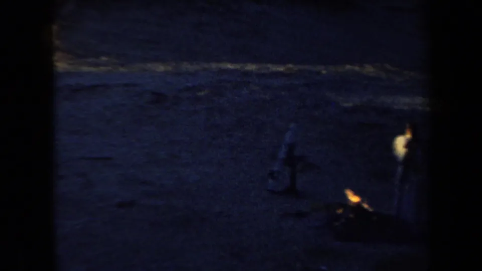 Low-light 1958 Arizona campsite view with dark sand and a small warm fire or lamp glow near the right side.