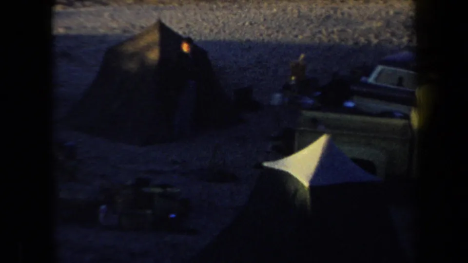 1958 Arizona home-movie frame showing tents and classic vehicles at a dim nighttime campsite.