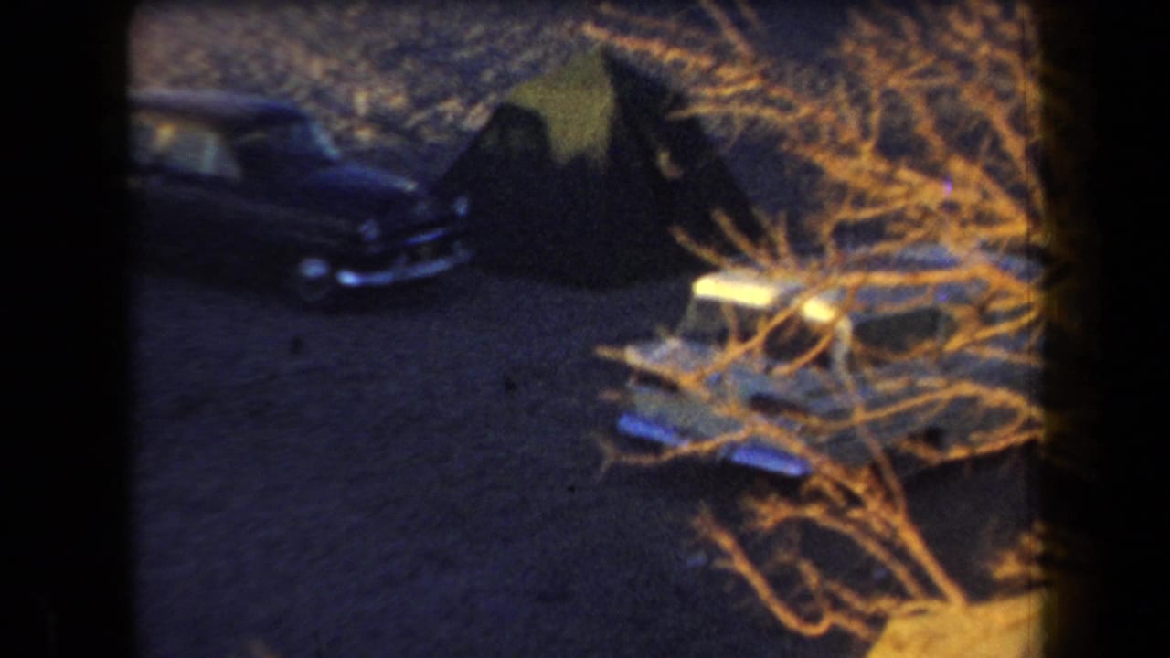 Dark nighttime campsite with a parked car, dry brush, and a tent-like form.