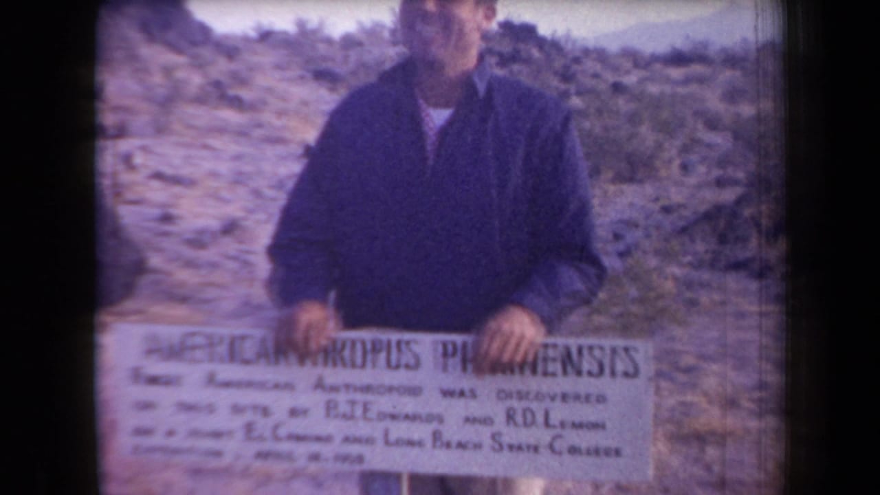In 1958 Arizona home-movie footage, a man faces the camera behind a sign reading AMERICANTHROPUS PIPKINENSIS in a rocky desert landscape.