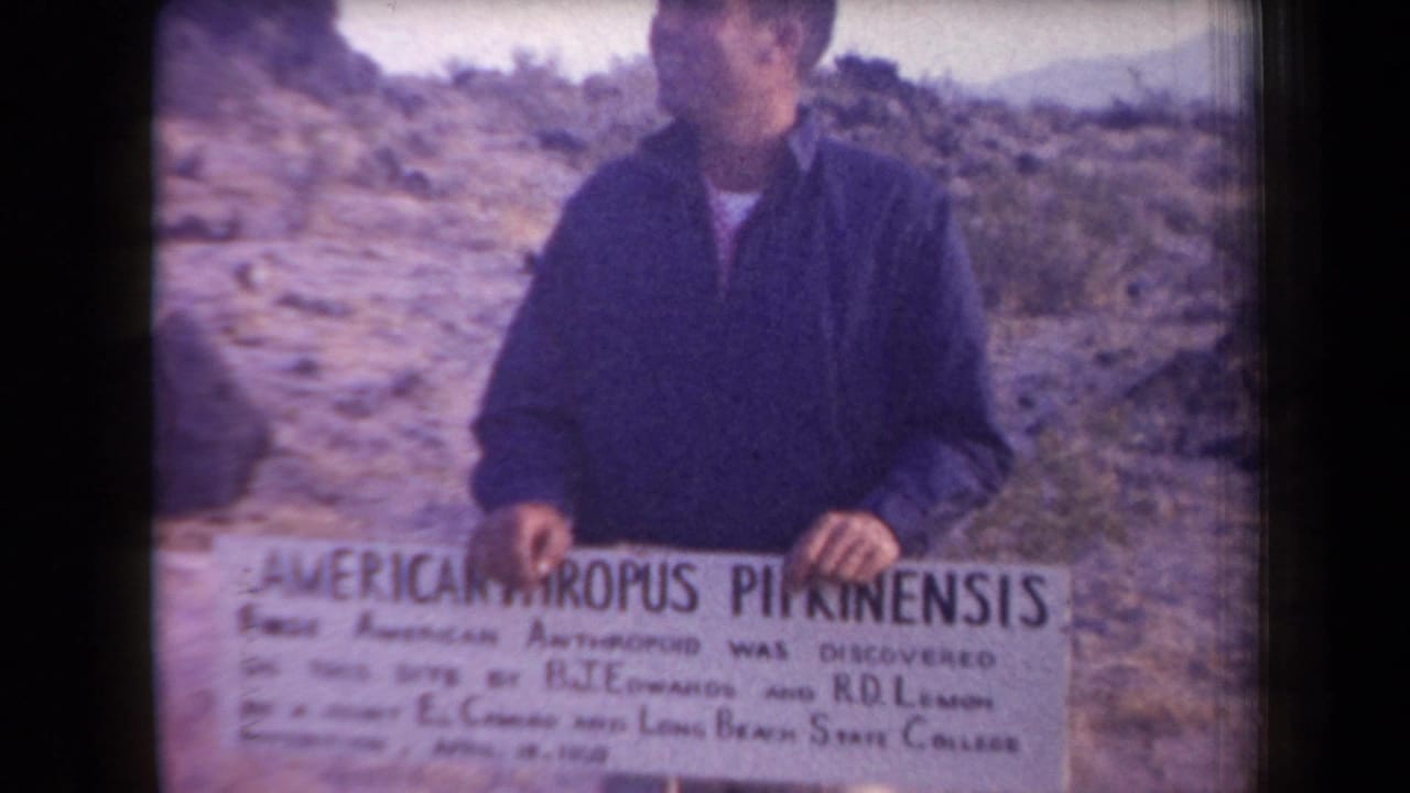 Man looks slightly to the side while holding a white discovery sign in the desert.