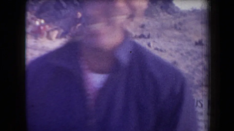 Close, motion-blurred 1958 Arizona frame of the man facing the camera with the fossil-site sign partly visible behind him.