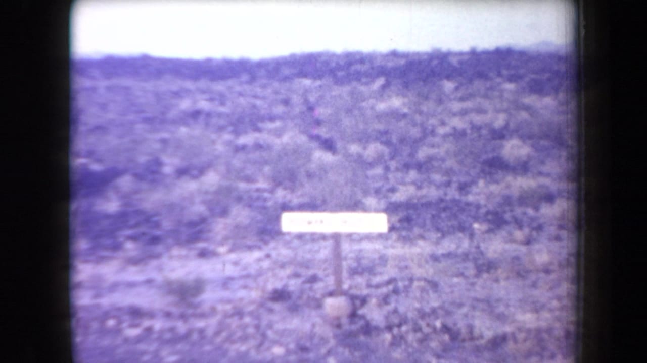 1958 Arizona 8mm frame showing a Hileman's Hole roadside sign in a sparse desert landscape.