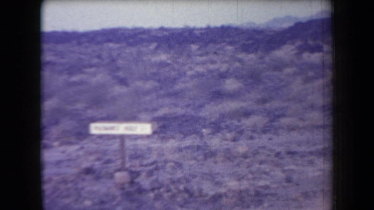 Soft 8mm view of the Hileman's Hole sign in an Arizona desert setting, with mountains in the distance.