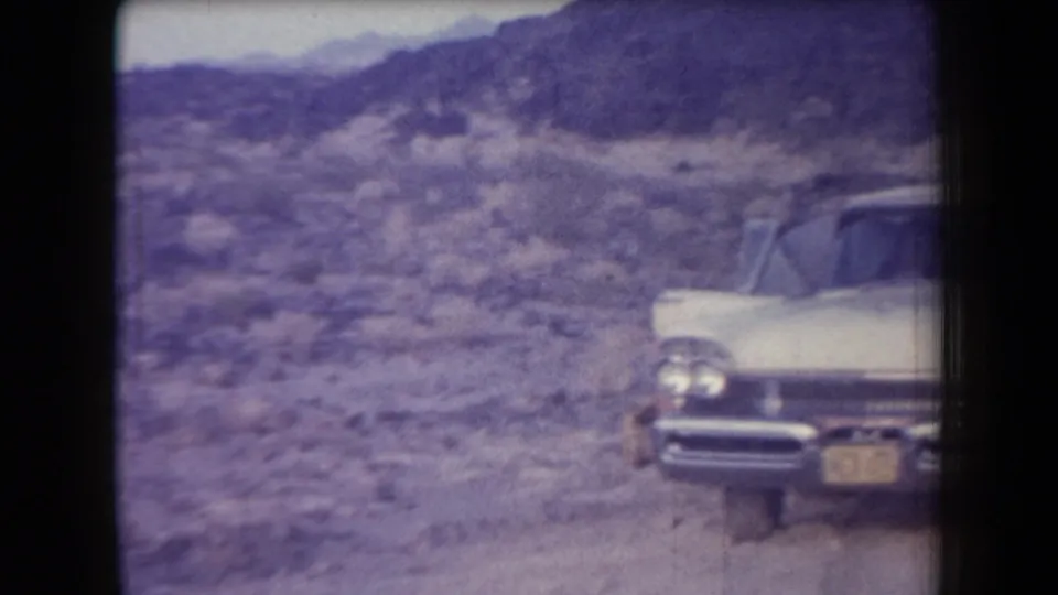 1958 Arizona home-movie frame showing a light-colored sedan stopped on a desert road, with one door open.