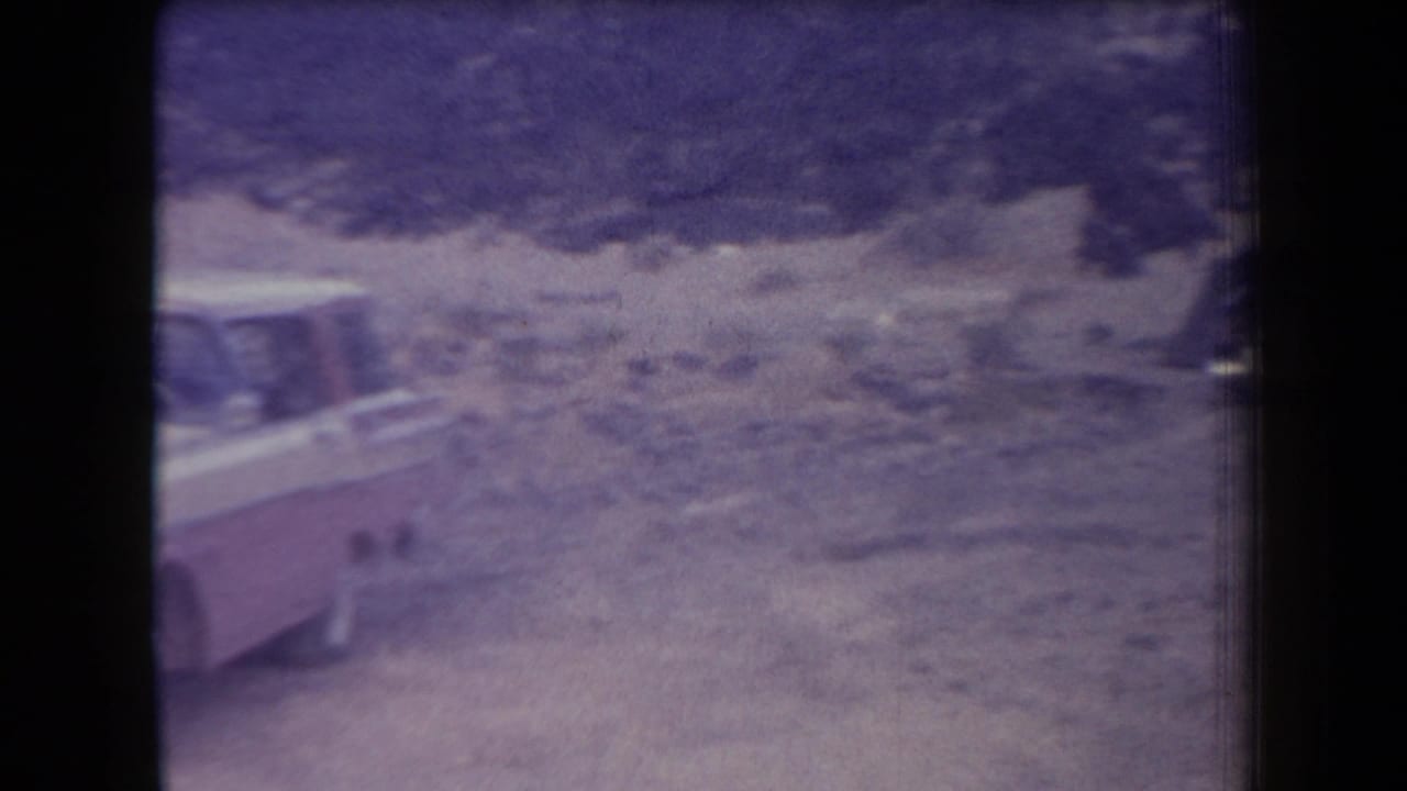 Two-tone vehicle partly visible on a rocky dirt parking area.
