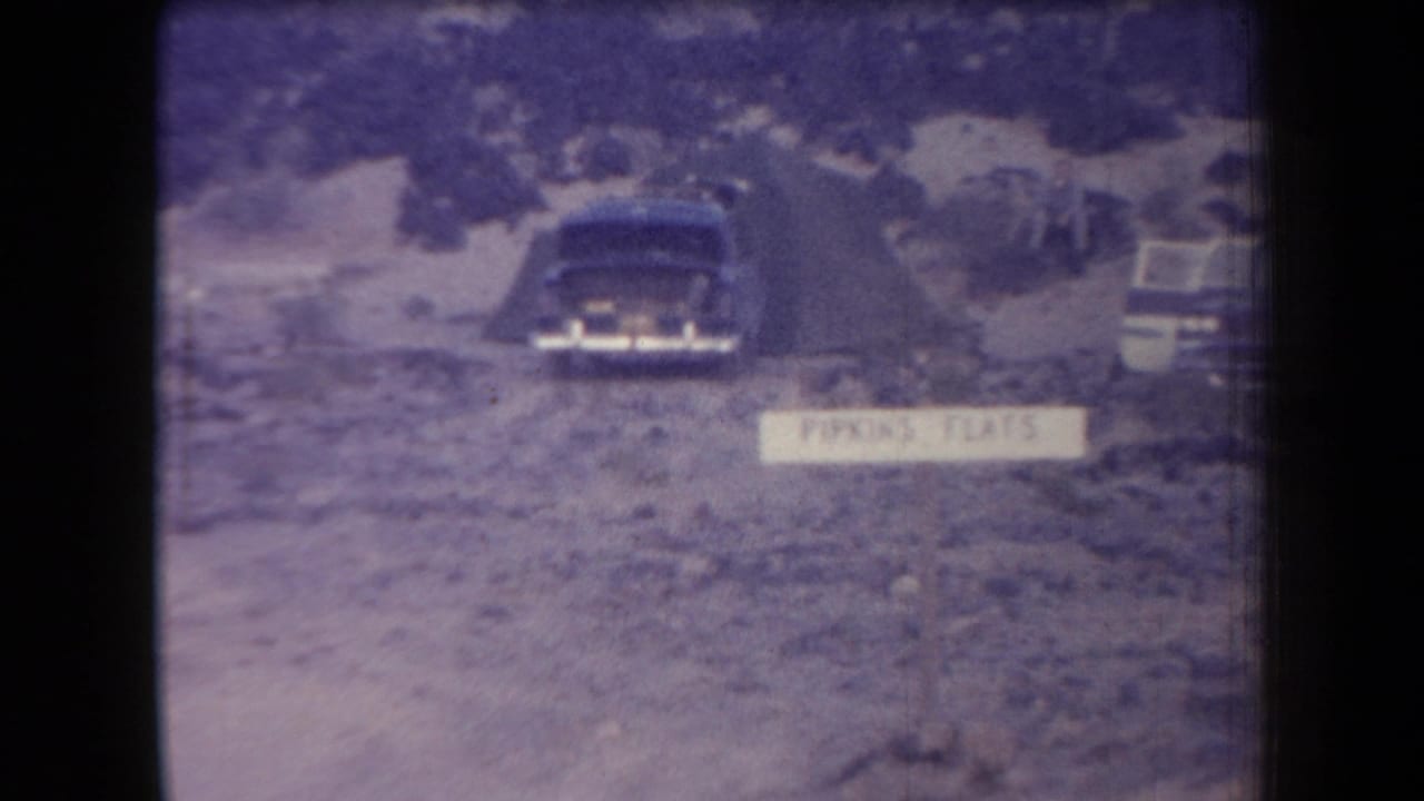1958 Arizona frame with a dark sedan, a white Parking Flats sign, and another vehicle on rocky open ground.