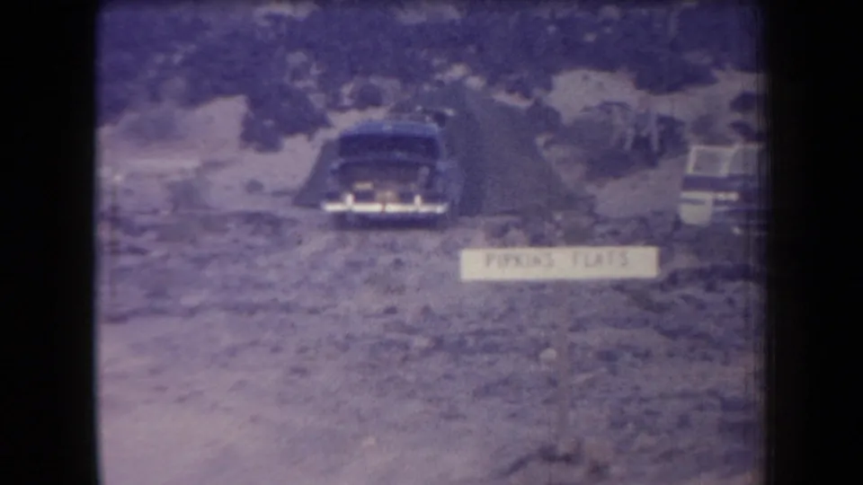 1958 Arizona frame with a dark sedan, a white Parking Flats sign, and another vehicle on rocky open ground.