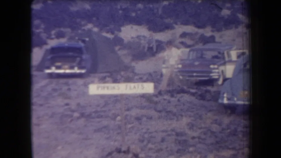 1958 Arizona home-movie frame showing multiple mid-century cars parked near a Parking Flats sign on uneven terrain.