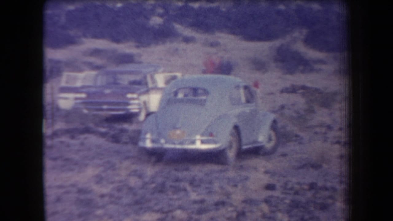 1958 Arizona home-movie frame showing classic cars parked in a rocky desert landscape with low hills beyond.