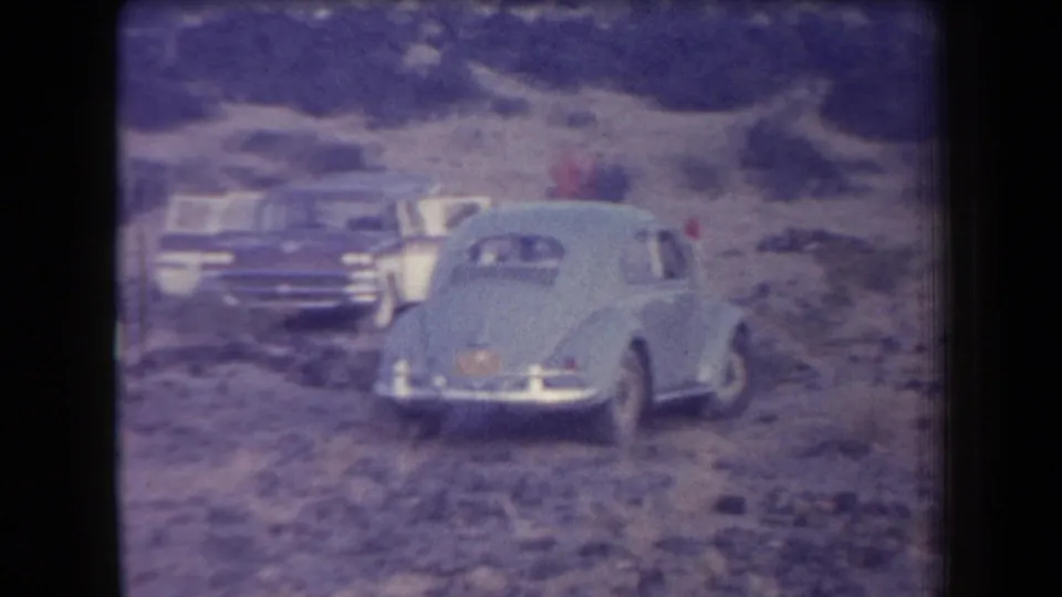 1958 Arizona home-movie frame showing classic cars parked in a rocky desert landscape with low hills beyond.