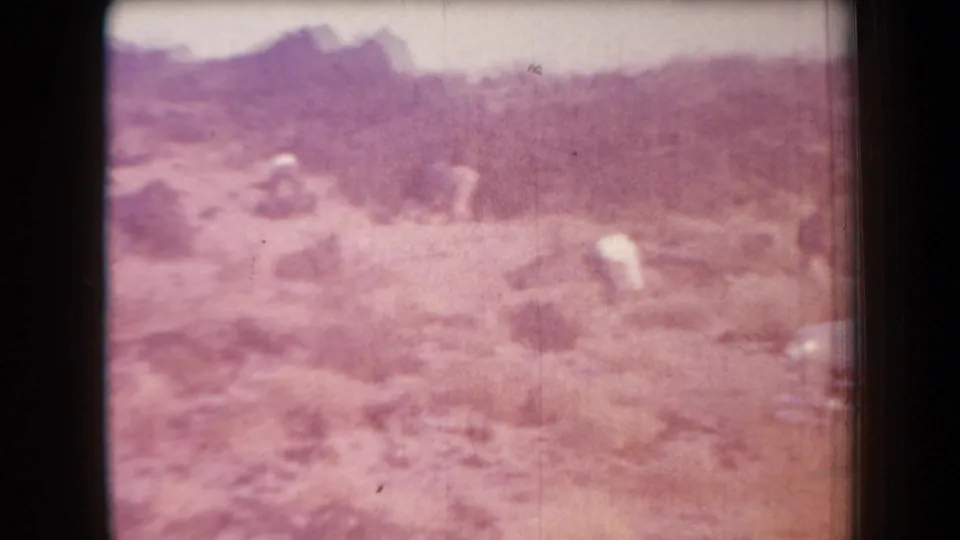 Blurred 1958 Arizona home-movie view of people moving through scrubby, rocky desert ground.
