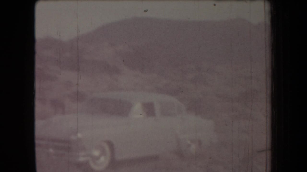 1958 Arizona 8mm frame showing a soft, faded view of a light-colored car against low arid hills.