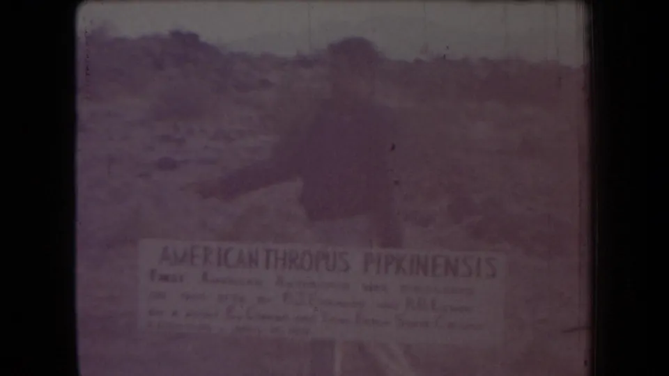 1958 Arizona 8mm frame with a partially legible AMERICANTHROPUS PIPKINENSIS sign in front of rocky desert terrain.