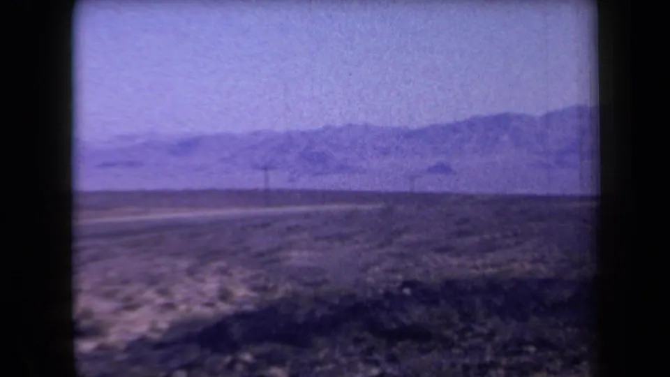 1958 Arizona 8mm frame showing a desert road, sparse shrubs, utility poles, and low mountains in the distance.