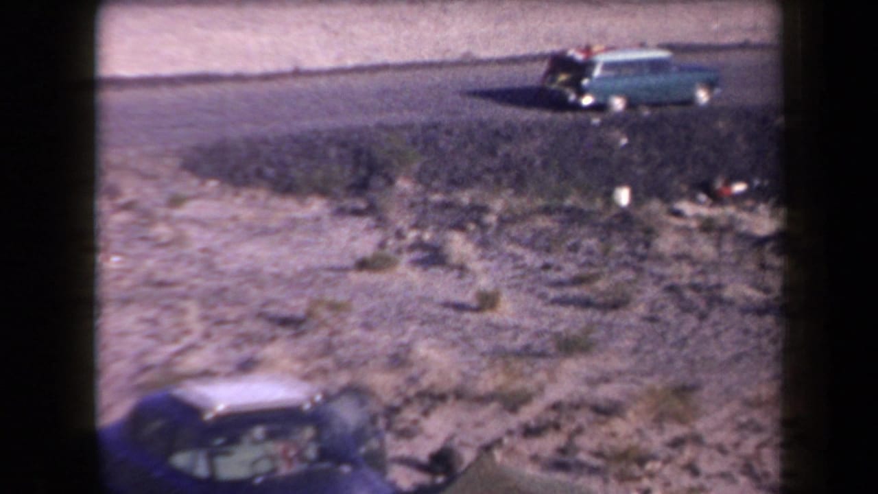 1958 Arizona roadside view with a turquoise station wagon in the distance and a dark blue sedan entering the lower foreground.