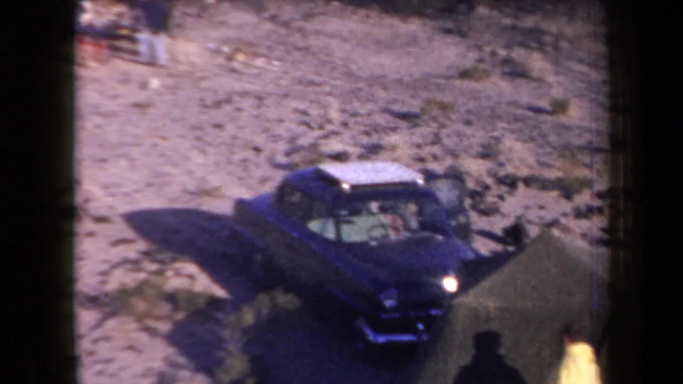 1958 Arizona home-movie frame showing a dark blue sedan parked near a tent on sandy desert terrain.