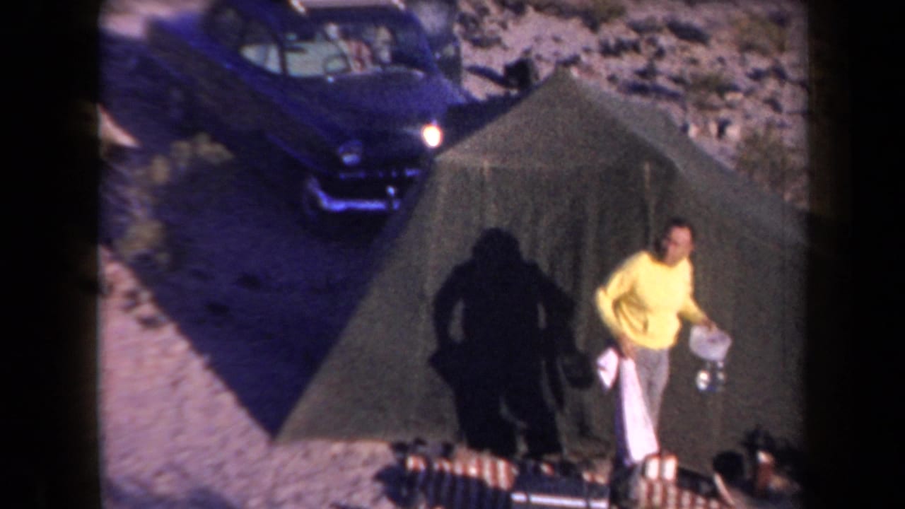 1958 Arizona home-movie frame showing a man in a yellow shirt beside a green canvas tent, with a dark classic car nearby.