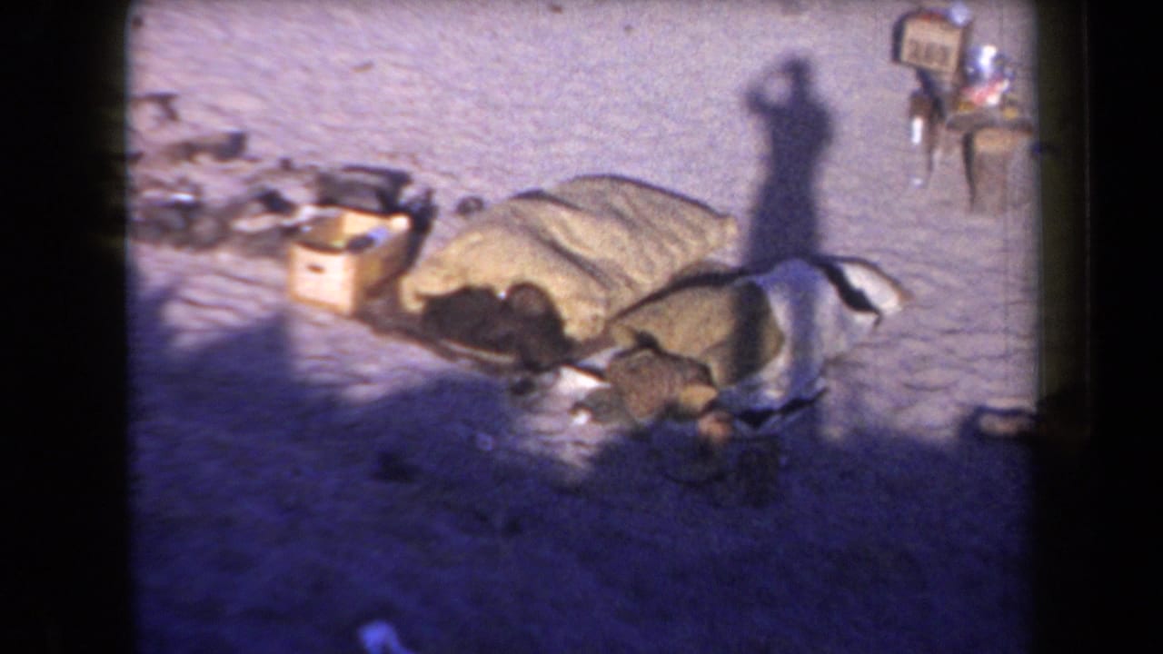 Desert campsite detail with sleeping bags, boxes, and scattered supplies in a 1958 Arizona home-movie frame.