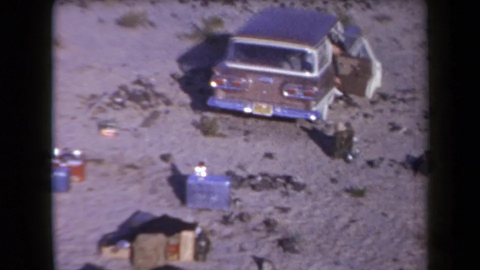 Classic station wagon parked beside scattered camping supplies at an Arizona desert campsite in 1958 footage.