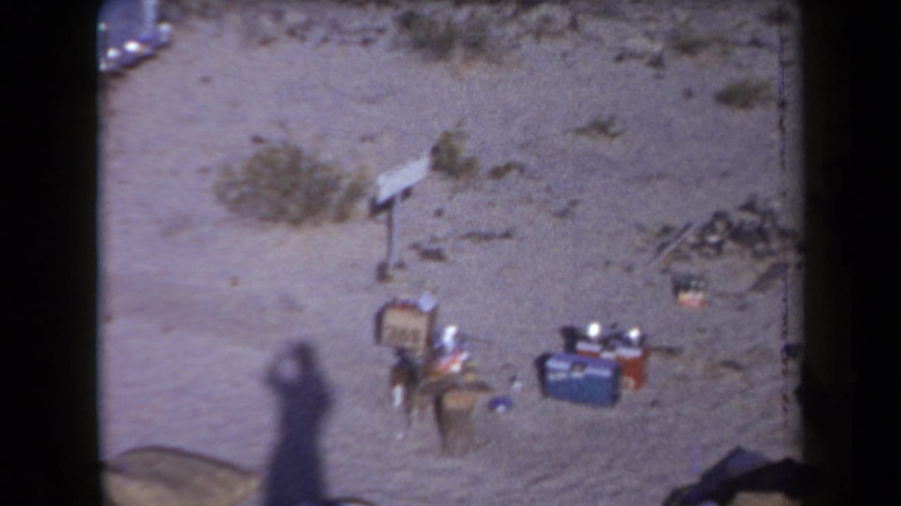 1958 Arizona 8mm frame showing luggage, coolers, and personal items scattered on sandy desert terrain near a roadside crash.