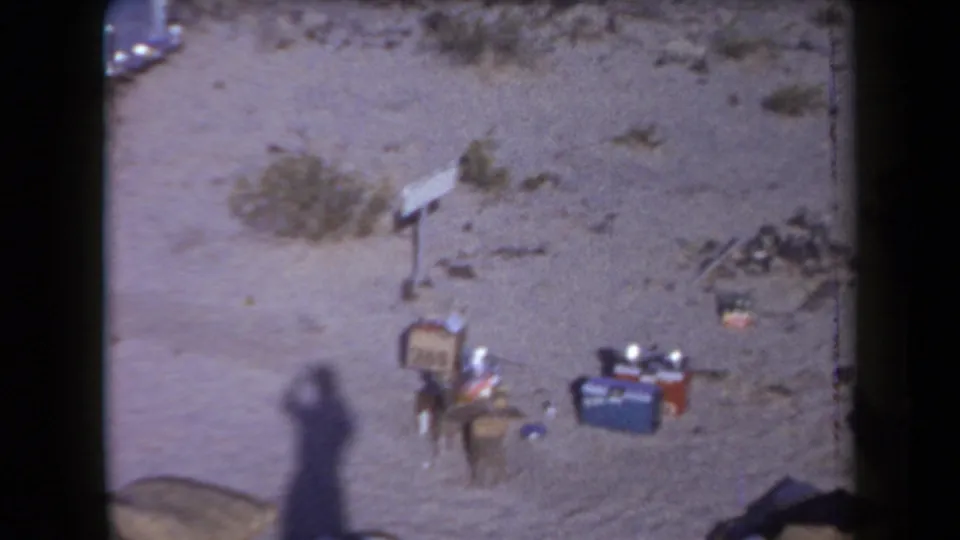 1958 Arizona 8mm frame showing luggage, coolers, and personal items scattered on sandy desert terrain near a roadside crash.