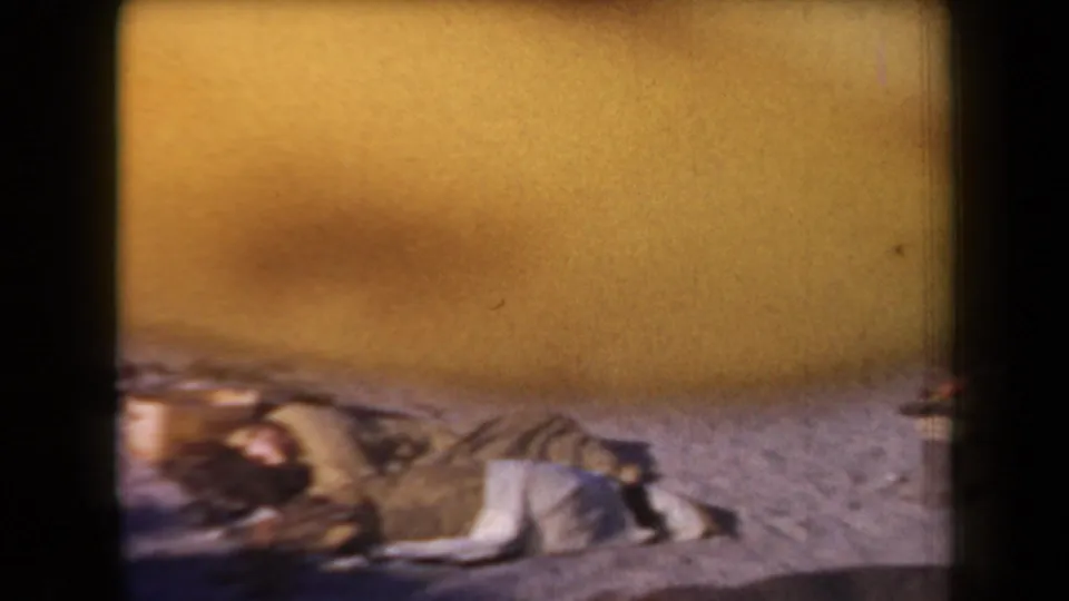 1958 Arizona 8mm frame with a blanket and belongings on sandy ground, partly obscured by yellow exposure flare and film edge.