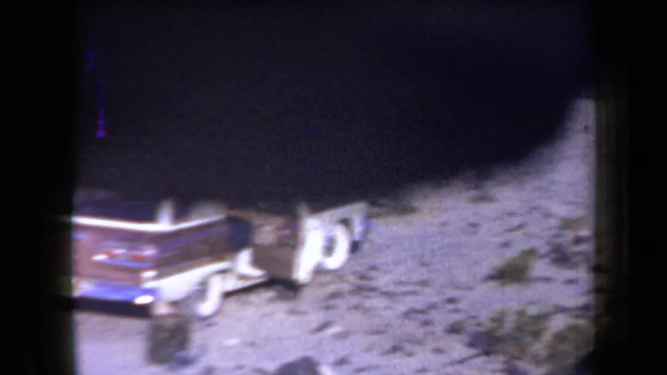 1958 Arizona desert camping frame with a parked station wagon, sandy ground, sparse brush, and strong shadowing from the 8mm scan.