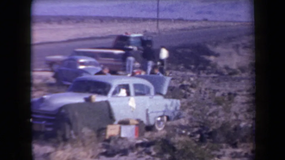 Roadside stop in Arizona, 1958 metadata, with light-colored sedans, a station wagon, people, and small items set out in desert terrain.