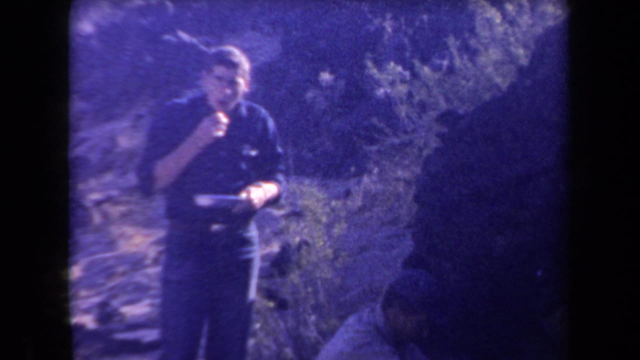 1958 Arizona frame of an adult man eating from a plate or dish while standing in soft-focused desert brush.