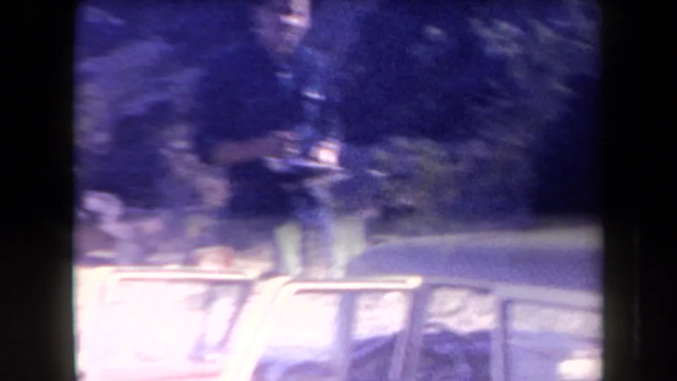1958 Arizona home-movie frame showing a man with a plate near a light-colored car, with desert brush and soft film blur.