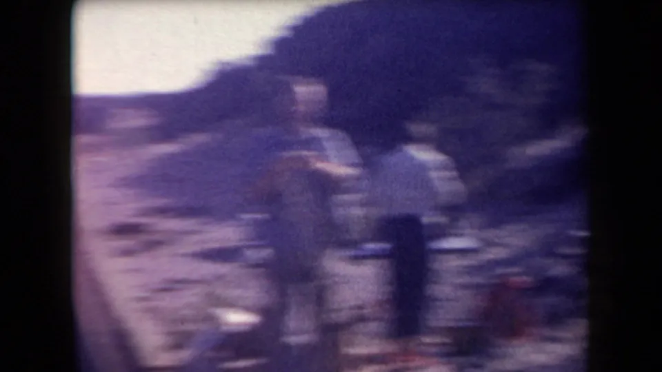 Soft, motion-blurred 8mm frame showing figures, vehicles, and roadside gear during the same desert outing.