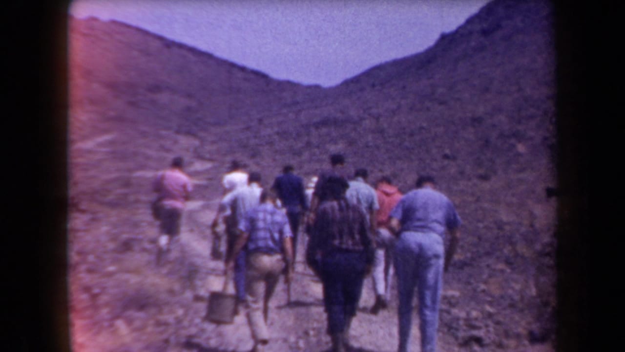 1958 Arizona 8mm frame showing adult hikers from behind on a steep dirt path in arid mountainous terrain.
