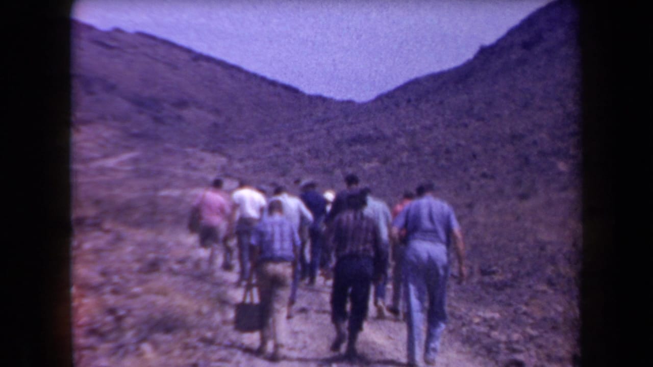 Hikers continue up a dirt trail with rocky hills rising on both sides.