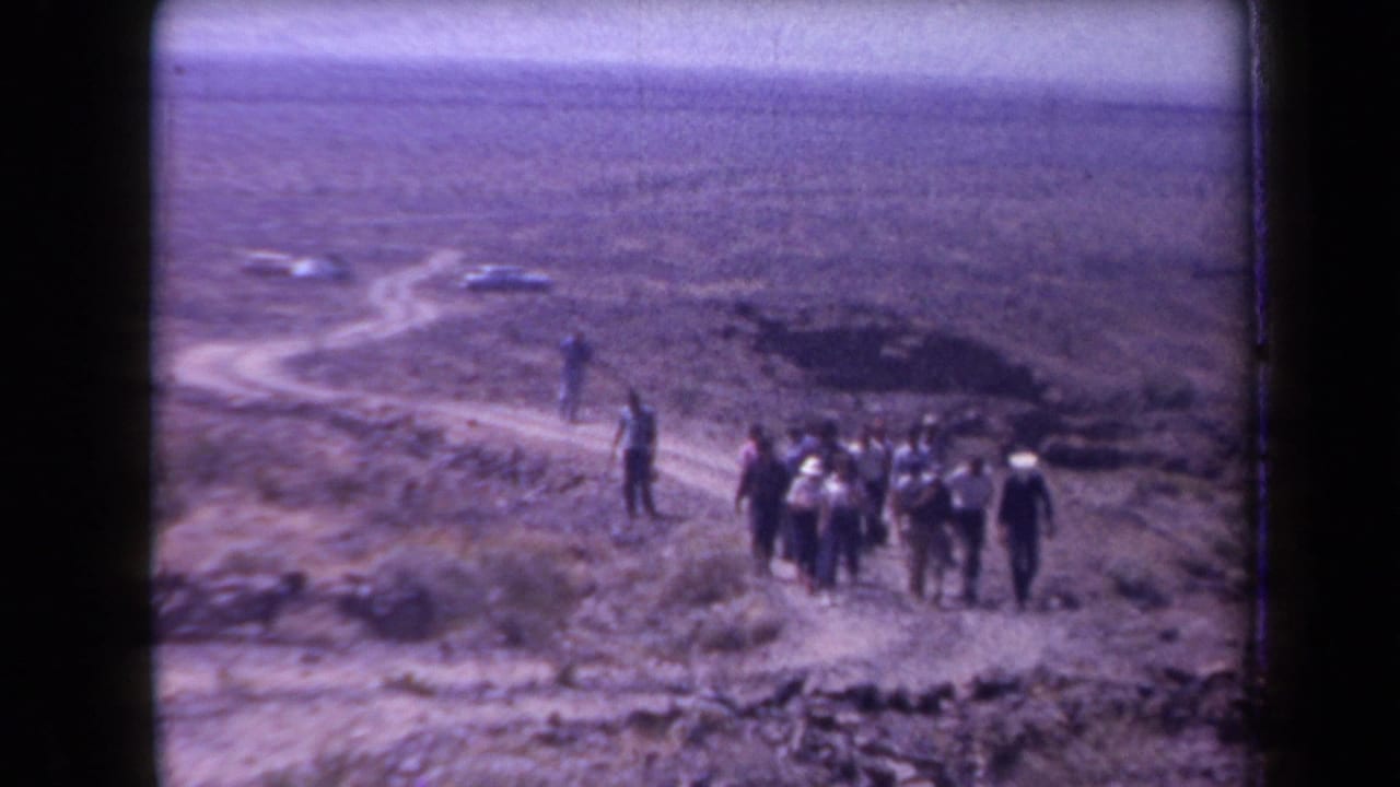 1958 Arizona desert scene with a group of men gathered on rocky terrain and a winding dirt road behind them.